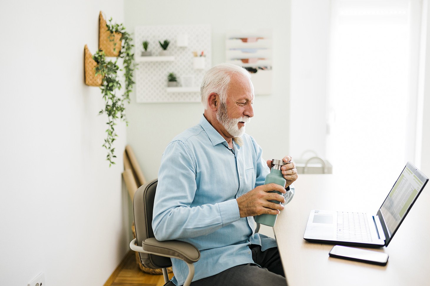 Portrait d'un senior assis à son bureau avec, entre ses mains, une gourde pour s’hydrater 