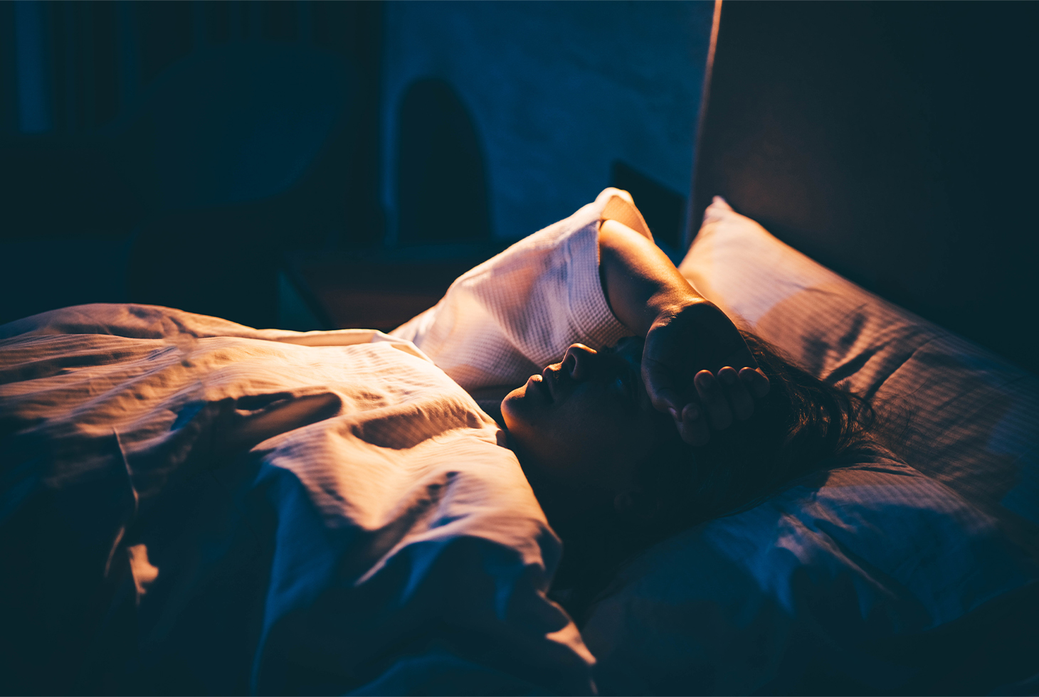 Portrait d’une femme allongée dans son lit soufrant d’insomnie. Visuel d’illustration pour la thématique de l’énurésie nocturne.