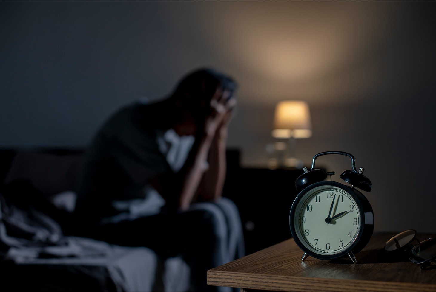 Portrait d’un homme assis sur son lit, la tête entre ses mains. Visuel pour illustrer les réveils nocturnes causés par la nycturie.