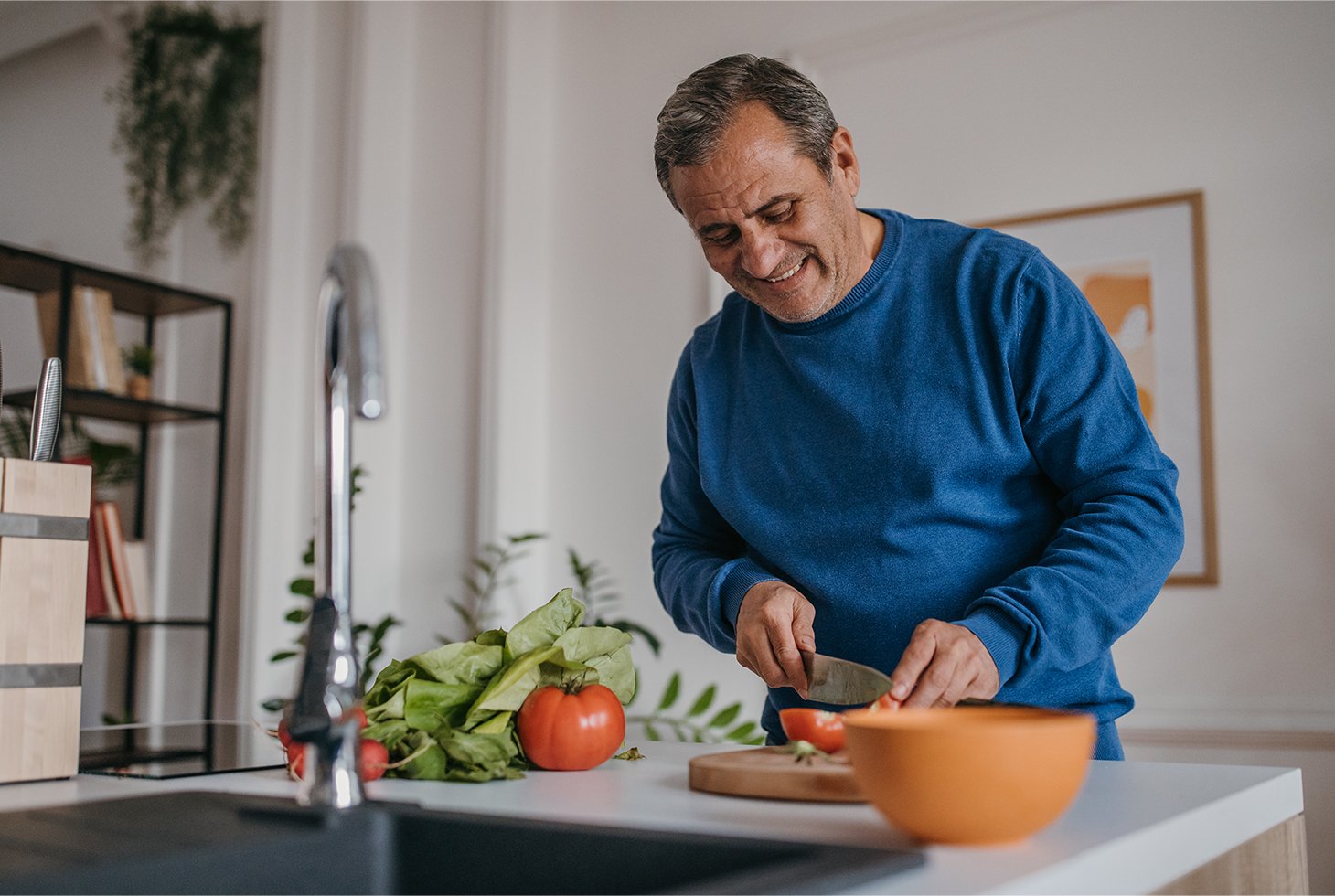 Un homme préparant une salade de crudités dans sa cuisine. Visuel d’illustration pour traiter du rôle joué par l’alimentation dans la réduction des fuites urinaires.