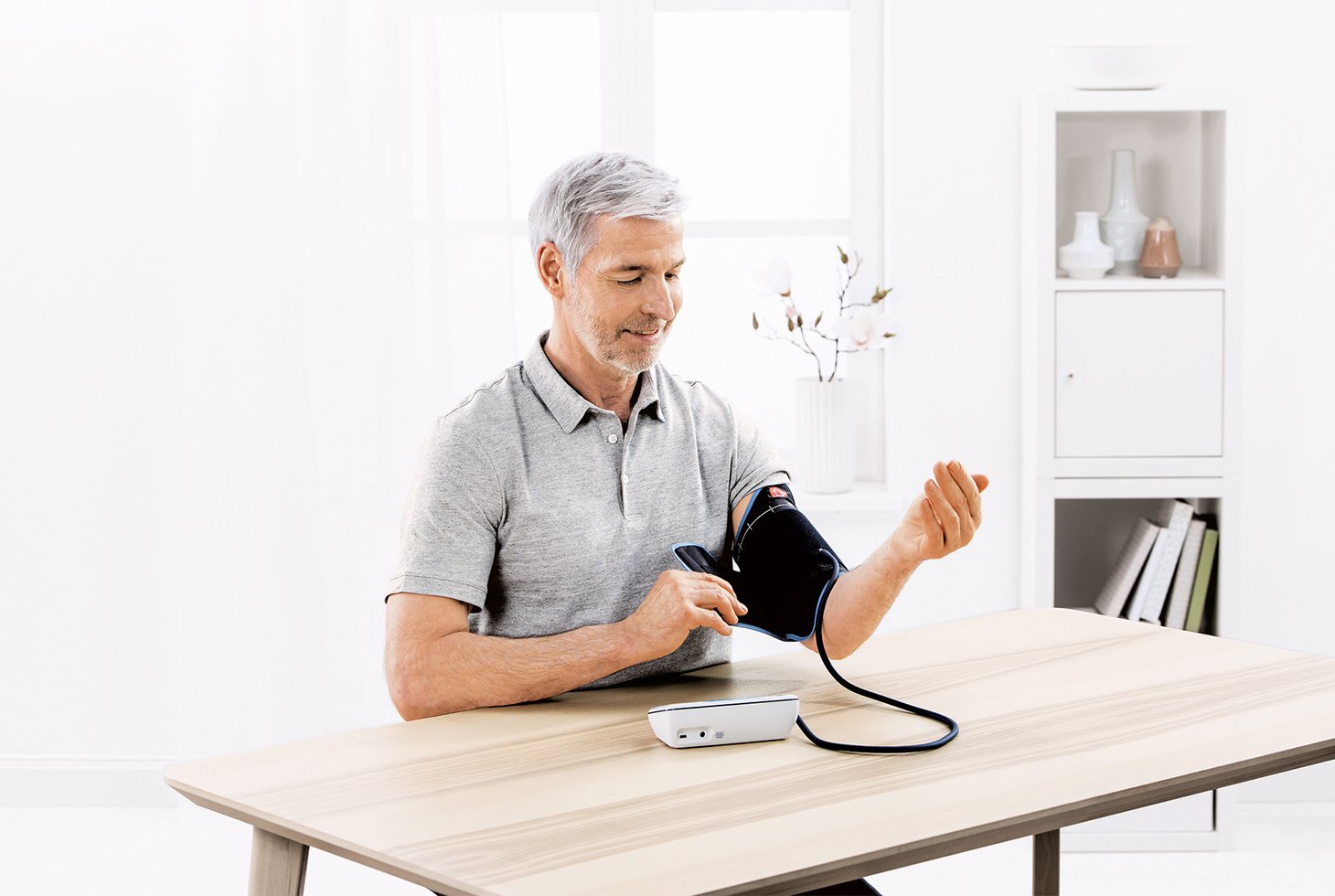 Un homme, assis, mesure sa pression artérielle à l’aide du tensiomètre connecté Veroval Duo control.