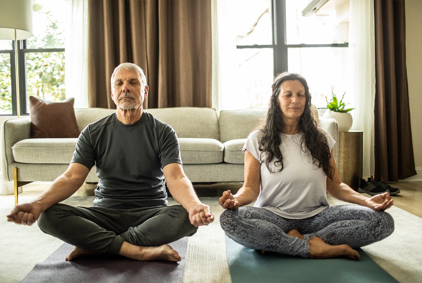 Un homme et une femme assis sur un tapis de yoga et effectuant la posture du lotus. Ce visuel illustre les bienfaits du yoga pour réduire l’incontinence liée au stress ou à l’effort.