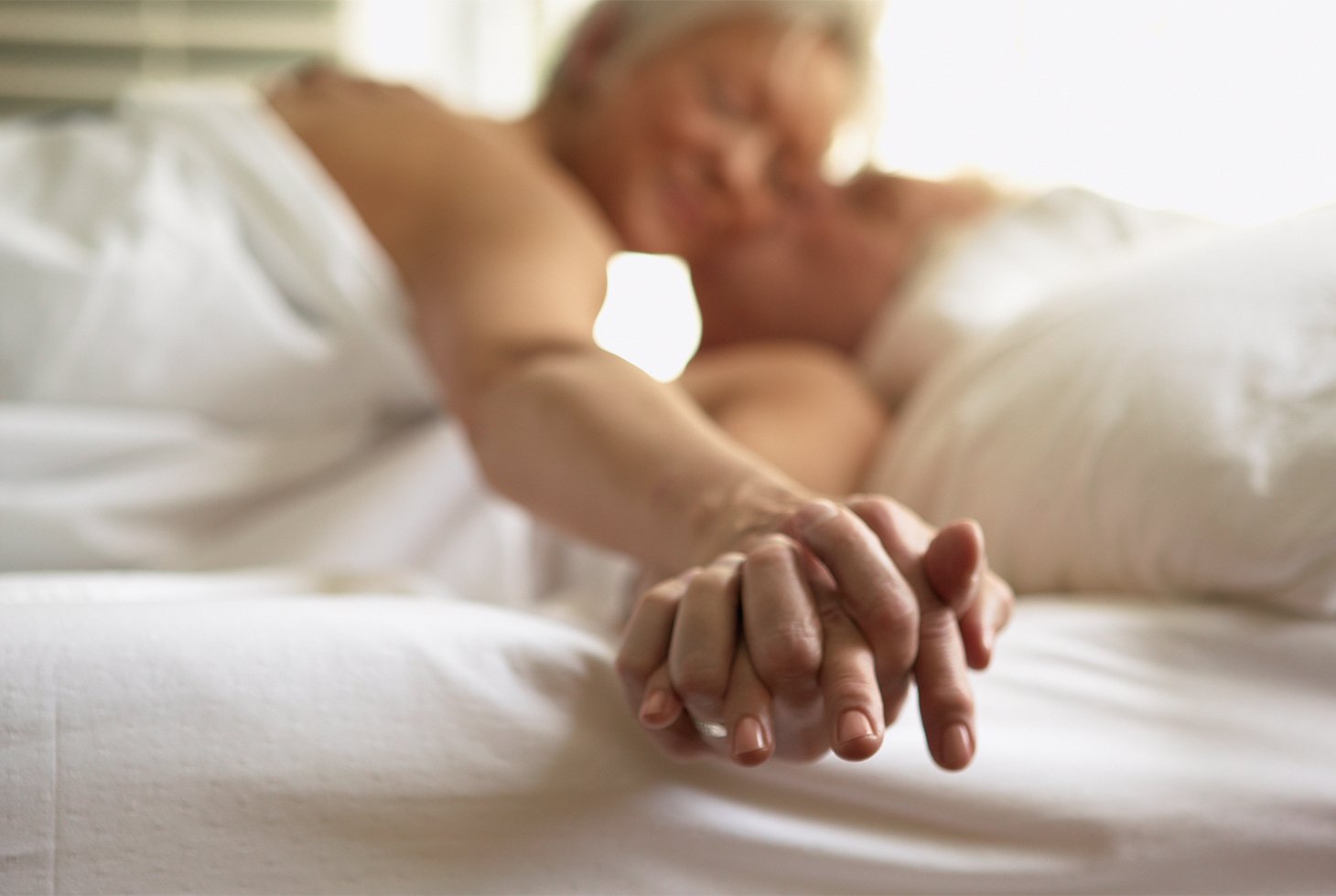 Un couple de seniors s’embrassant et se tenant la main dans un lit. Visuel pour illustrer une sexualité épanouie malgré des fuites urinaires. 
